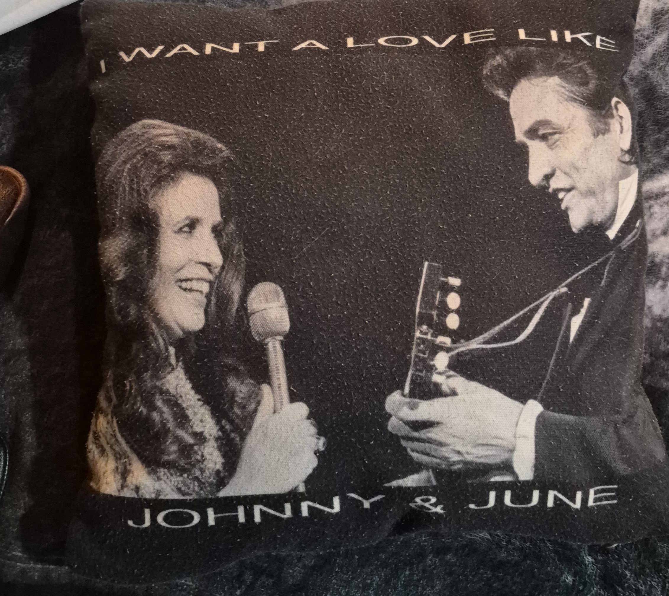 A decorative pillow featuring a black and white image of a woman holding a microphone and a man playing a guitar, with the text 'I WANT A LOVE LIKE JOHNNY & JUNE'.