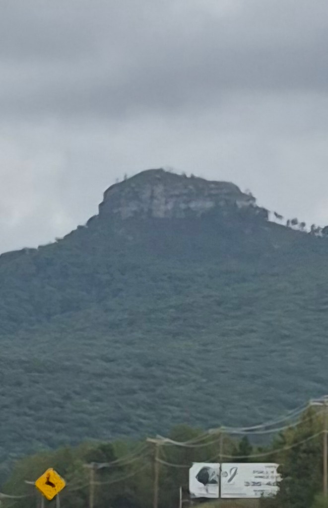 A prominent mountain peak with a flat top rises above the surrounding landscape, set against a cloudy sky.