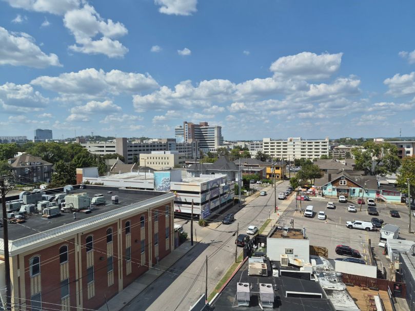 A cityscape view showing a mix of modern buildings and older structures, with a blue sky filled with clouds.